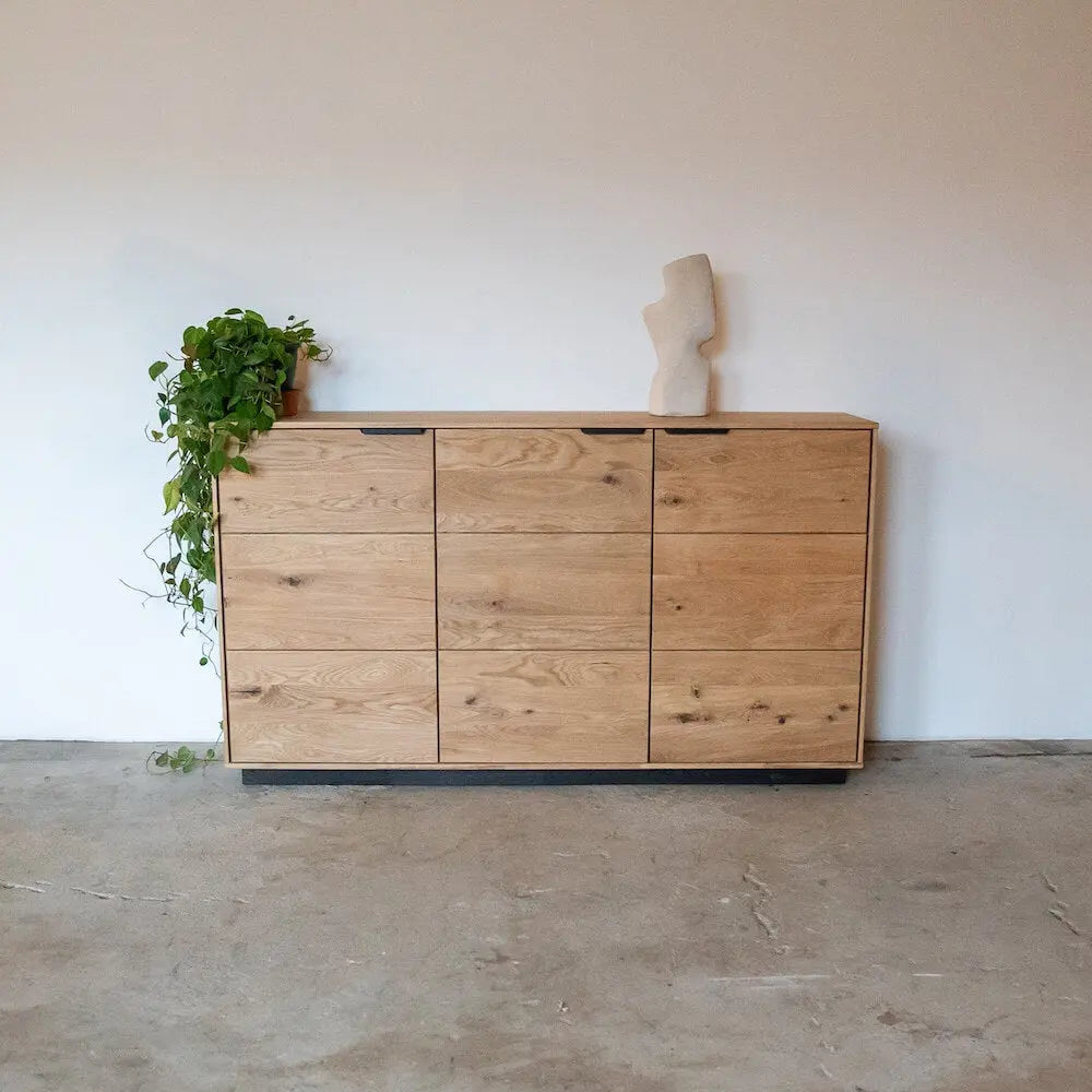 Massive Eichenholz-Kommode mit schwarzem Sockel, minimalistisches Design, links mit Kletterpflanze.