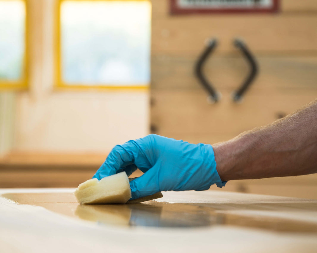 Holz richtig ölen – Hand trägt mit Schwamm Öl auf Massivholz auf, für langlebige Möbelpflege und Schutz.