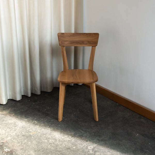 Esszimmerstuhl aus Massivholz Eiche mit geschwungener Lehne auf Sichtbeton vor heller Wand