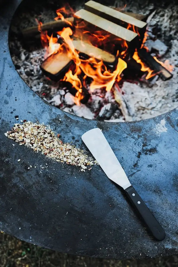 Feuerring mit offener Flamme, Spatel und Gewürzen – Outdoor-Kochen mit woodcuisine Naturküche.